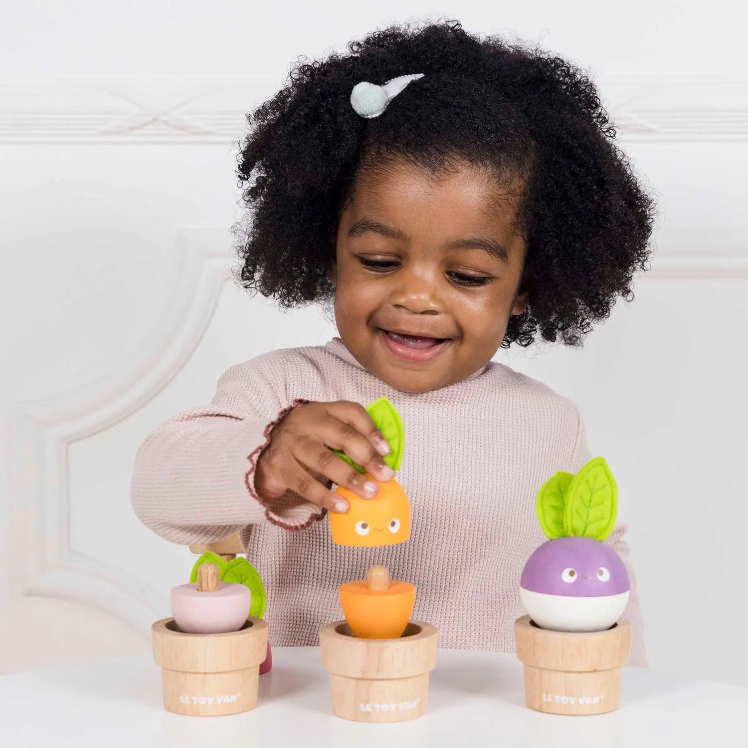 Een vrolijke set van Le Toy Van met drie soorten houtachtige groenten in natuurlijke houten potten - spelend meisje